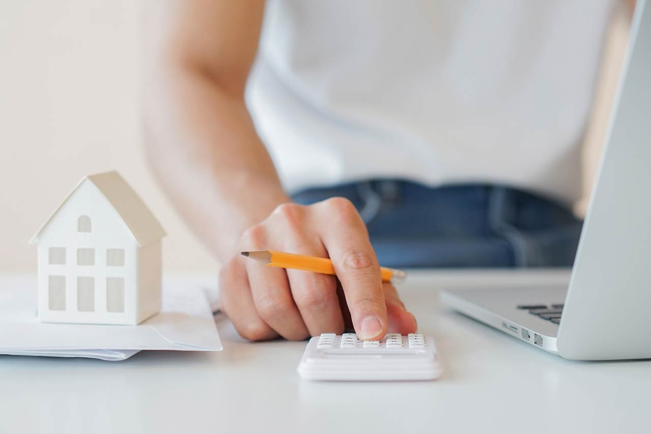 Close up of a mans hand with a pencil calculating with a small home model