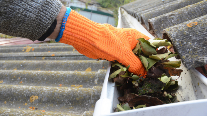 Roofer cleaning a rain gutter with an orange glove on Roofer cleaning a rain gutter with an orange glove on