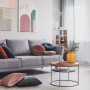 Real photo of abstract paintings hanging on white wall above a gray sofa in a living room interior with big windows