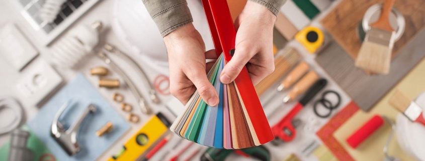 Male hands holding swatches and choosing the right color, work tools on background top view