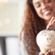 happy young mixed race woman holding a piggybank and depositing a coin as savings