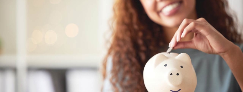 happy young mixed race woman holding a piggybank and depositing a coin as savings