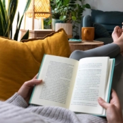 young woman relaxing at home reading a book lying on sofa