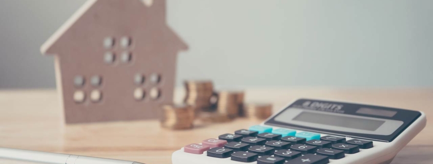 Calculator with wooden house and coins stack and pen on wood table