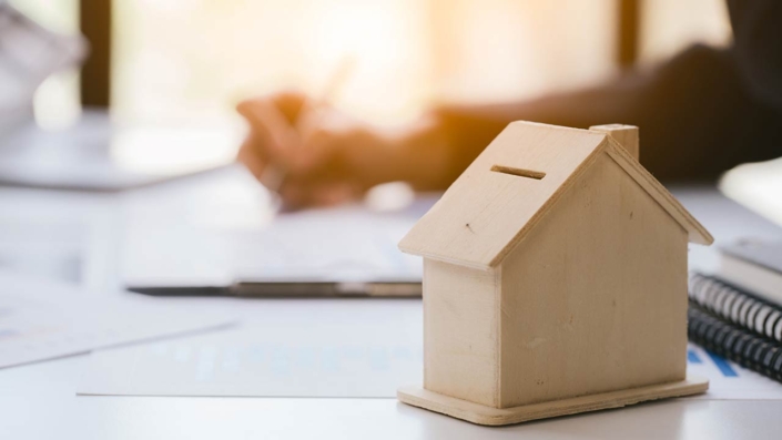 Close up and focus of house model mock up. Blur working hand is holding pen and writing is background Close up and focus of house model mock up. Blur working hand is holding pen and writing is background