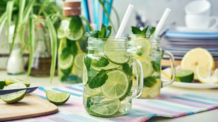 Two glasses and a bottle of homemade lemon, lime, and mint lemonade sit on the wooden dining table Two glasses and a bottle of homemade lemon, lime, and mint lemonade sit on the wooden dining table