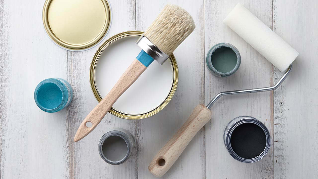 Paint brush, sponge roller, paints, waxes and other painting or decorating supplies on white wooden planks