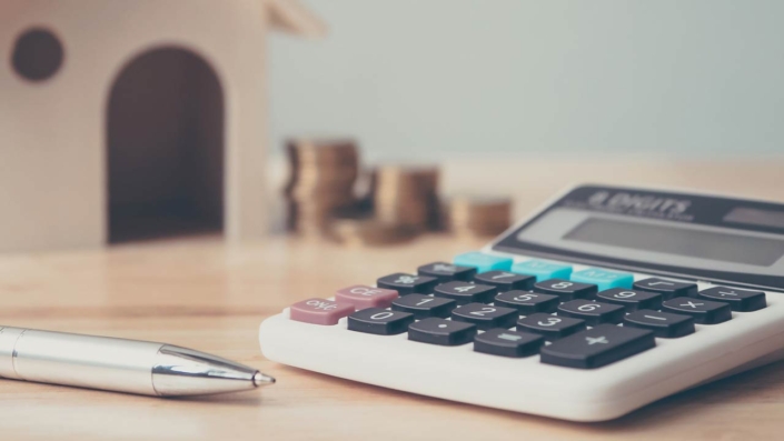 Calculator with wooden house and coins stack and pen on wood table Calculator with wooden house and coins stack and pen on wood table